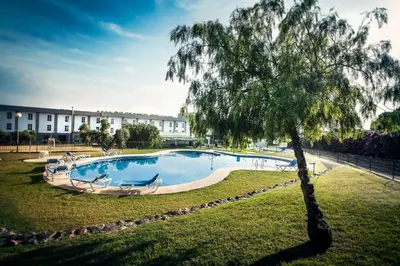 a swimming pool in a park with a tree at Gran Hotel Ciudad Del Sur in Puerto Real