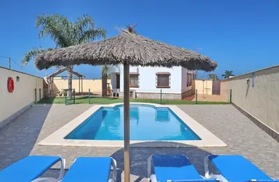 a swimming pool with a straw umbrella and chairs at Chalet Vigía 114 in Conil de la Frontera