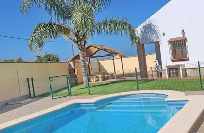 a swimming pool in front of a house with a palm tree at Chalet Vigía 114 in Conil de la Frontera