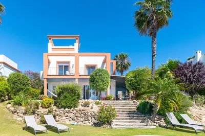 a house on the beach with chairs and palm trees at Villa Golf Sanlucar in Sanlúcar de Barrameda