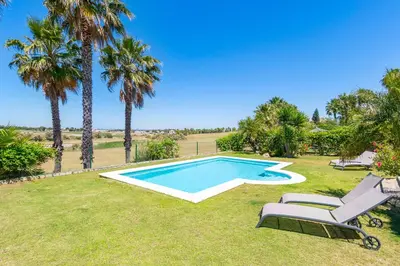 a swimming pool in a yard with palm trees at Villa Golf Sanlucar in Sanlúcar de Barrameda
