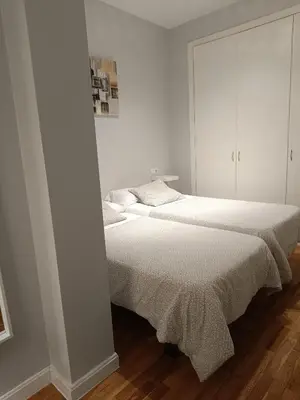 two beds in a bedroom with white walls and wood floors at Apartamentos Aloha 2 Centro El Puerto de Santa Maria in El Puerto de Santa María