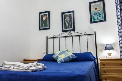 a bedroom with a bed with blue sheets and pictures on the wall at Apartamento La carraca in Chipiona
