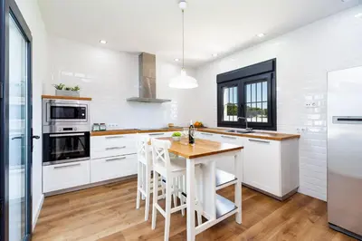 a kitchen with white cabinets and a wooden table at Villa La Barrosa in Chiclana de la Frontera