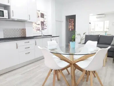 a white kitchen with a glass table and white chairs at Apartamento Marina el Puerto in El Puerto de Santa María