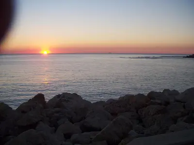 a sunset over the ocean with rocks on a beach at Apartamento Caballo Sherry in El Puerto de Santa María