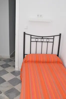 a bed with an orange comforter in a room at Pensión Las Cuatro Naciones in Cádiz