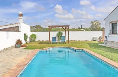 a swimming pool with two blue chairs next to a house at Casa con piscina 92 in Conil de la Frontera