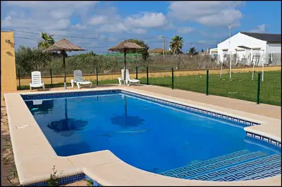 a large swimming pool with two chairs and a fence at Bungalow en complejo I in Conil de la Frontera