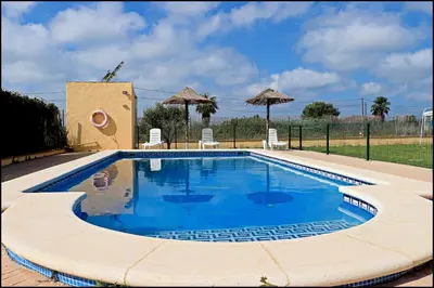 a swimming pool in a yard with chairs and umbrellas at Bungalow en complejo I in Conil de la Frontera