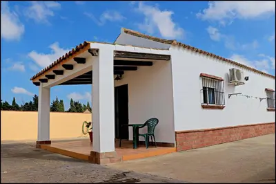 a small white house with a chair on a porch at Bungalow en complejo I in Conil de la Frontera