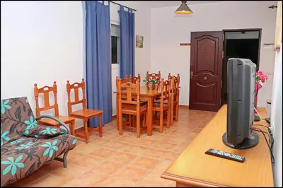 a living room with a television and a table with chairs at Bungalow en complejo I in Conil de la Frontera