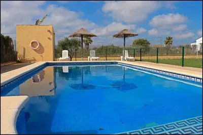 a large blue swimming pool with chairs and umbrellas at Bungalow en complejo II in Conil de la Frontera