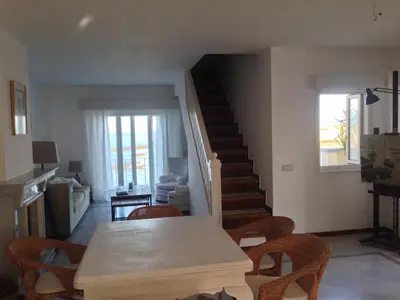 a living room with a table and chairs and a staircase at Ático Playa Muralla in El Puerto de Santa María