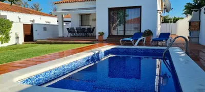a swimming pool with two blue chairs next to a house at Chalet Las Adelfas Chaparrillo in Conil de la Frontera