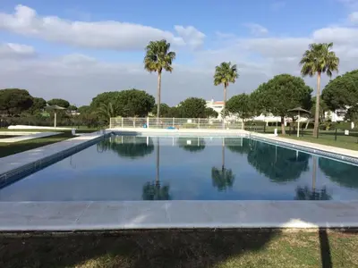 a swimming pool with palm trees in the background at Apartamento Retama Golf I in Chiclana de la Frontera