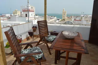 a table and two chairs on a balcony with a lighthouse at Apartamento El Mirador de Cadiz in Cádiz