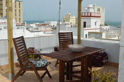 a wooden table and chairs on a balcony with a lighthouse at Apartamento El Mirador de Cadiz in Cádiz