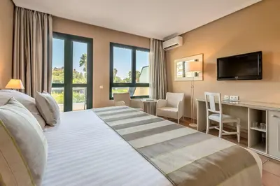 a bedroom with a large bed with a desk and a television at Barceló Jerez Montecastillo & Convention Center in Jerez de la Frontera