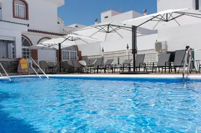 a swimming pool with chairs and umbrellas on a building at Hotel Chipiona in Chipiona