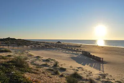 a pier on a beach with the sun in the distance at Tranvía Beach House in Chipiona