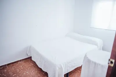 a room with a white bed and a stool at Casa Cordoba in Chipiona