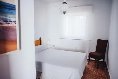 a bedroom with a white bed and a chair at Casa Cordoba in Chipiona
