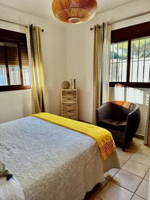 a bedroom with a bed and a chair and windows at Chalet Nora in Chiclana de la Frontera