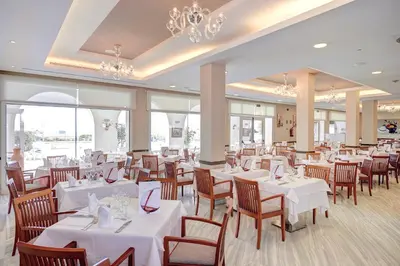 a dining room with white tables and chairs and chandeliers at Hipotels Flamenco Conil in Conil de la Frontera