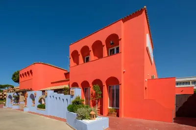 a red building with a white fence in front of it at Aparthotel las Dunas in Chiclana de la Frontera