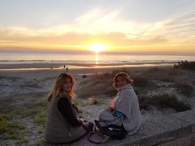 two girls sitting on the beach watching the sunset at El Campanario in Chiclana de la Frontera