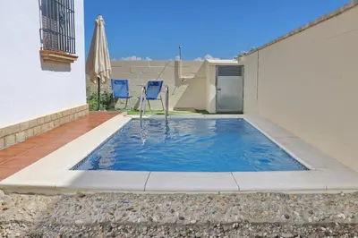 a small swimming pool with an umbrella and chairs at Chalet Chaparrillo Conil in Conil de la Frontera