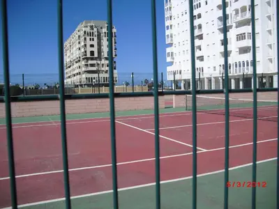 a tennis court seen through a fence with buildings at Apartamento Valdelagrana in El Puerto de Santa María