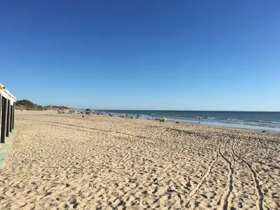 a sandy beach with a building and the ocean at Atico Costa Ballena golf y playa parking&wifi in Costa Ballena