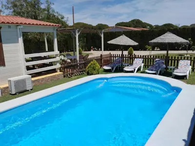 a blue swimming pool with chairs and umbrellas at Cabaña Blanca Roche Jorge in Conil de la Frontera