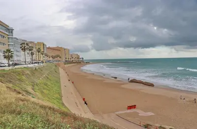 a beach with buildings and the ocean on a cloudy day at Apartamento Andujar in Cádiz
