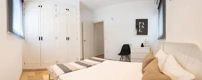 a white bedroom with a bed and a chair at Moderno Apartamento junto a la Playa in Sanlúcar de Barrameda
