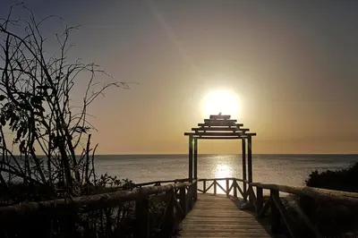 a wooden pathway leading to the ocean with the sun setting at Summerland Apartments Rota in Rota