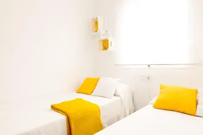 two beds with yellow pillows in a white room at Summerland Apartments Rota in Rota