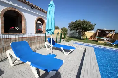 two blue chairs and an umbrella next to a swimming pool at Casa Melli in Conil de la Frontera