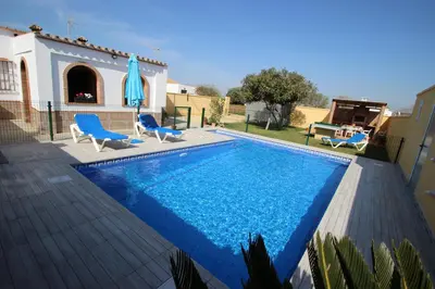 a swimming pool with two chairs and an umbrella at Casa Melli in Conil de la Frontera
