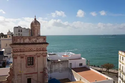 a building with a clock tower next to the ocean at Hotel Casa de las Cuatro Torres in Cádiz