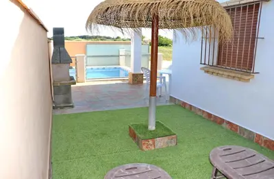 a patio with a grass umbrella and a pool at Chalet Peñuelas in Conil de la Frontera