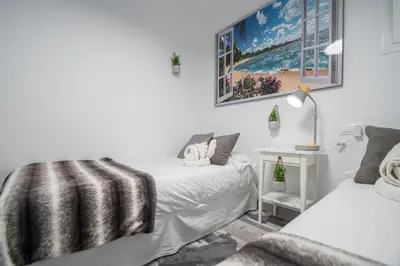 a white bedroom with two beds and a lamp at Apartamento Arco de los Blanco in Cádiz