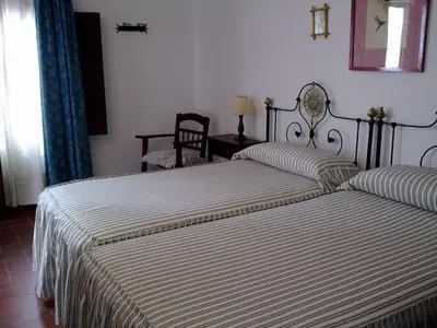 a bedroom with two beds and a chair and a window at Hostal Gran Capitan in Chipiona