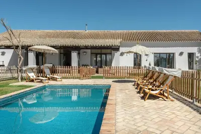 a pool with chairs and umbrellas next to a house at HACIENDA LAS MESAS - Luxury Villa Jerez in Jerez de la Frontera