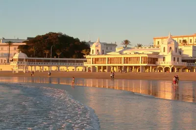 people walking on the beach in front of a building at Gades Suite in Cádiz