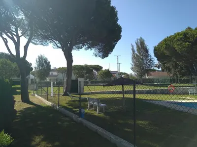 a fence with a bench in a park with trees at Chalet en Roche in Conil de la Frontera