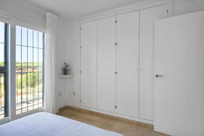 a white bedroom with white wardrobes and a window at Adosado Dulce Barrosa in Chiclana de la Frontera
