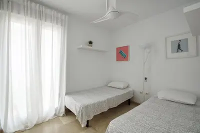 a white room with two beds and a window at Adosado Dulce Barrosa in Chiclana de la Frontera